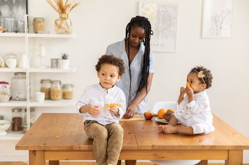 Free Mother with kids enjoying fruit in a bright family kitchen. Warm, cozy atmosphere. Stock Photo