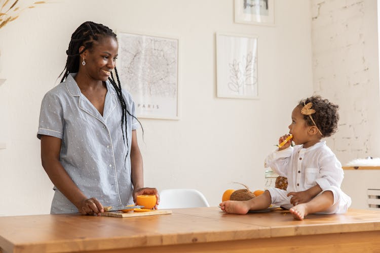 Mother Smiling To Child Eating Orange