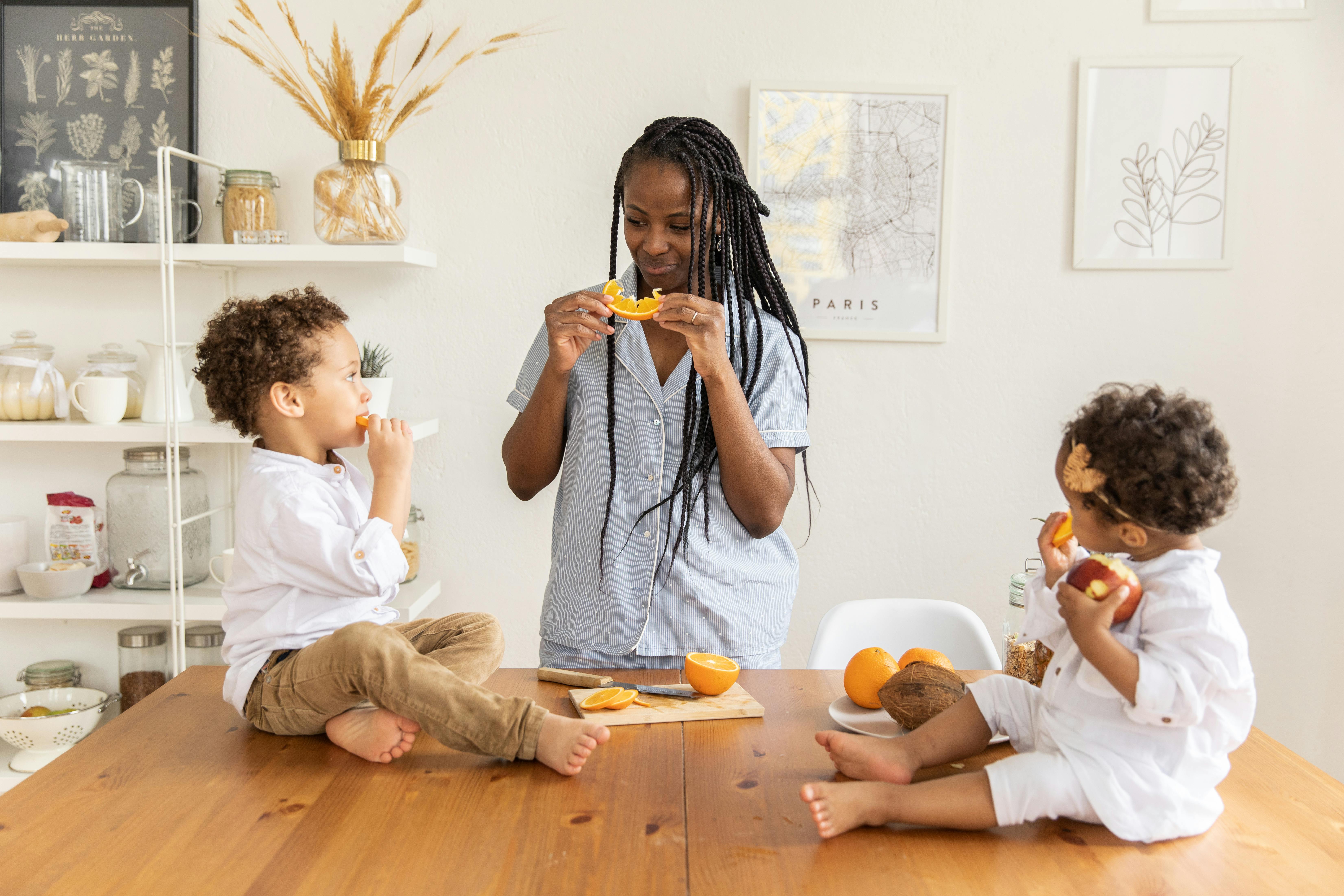Free Girl in White Long Sleeve Shirt Eating Orange Fruit Stock Photo