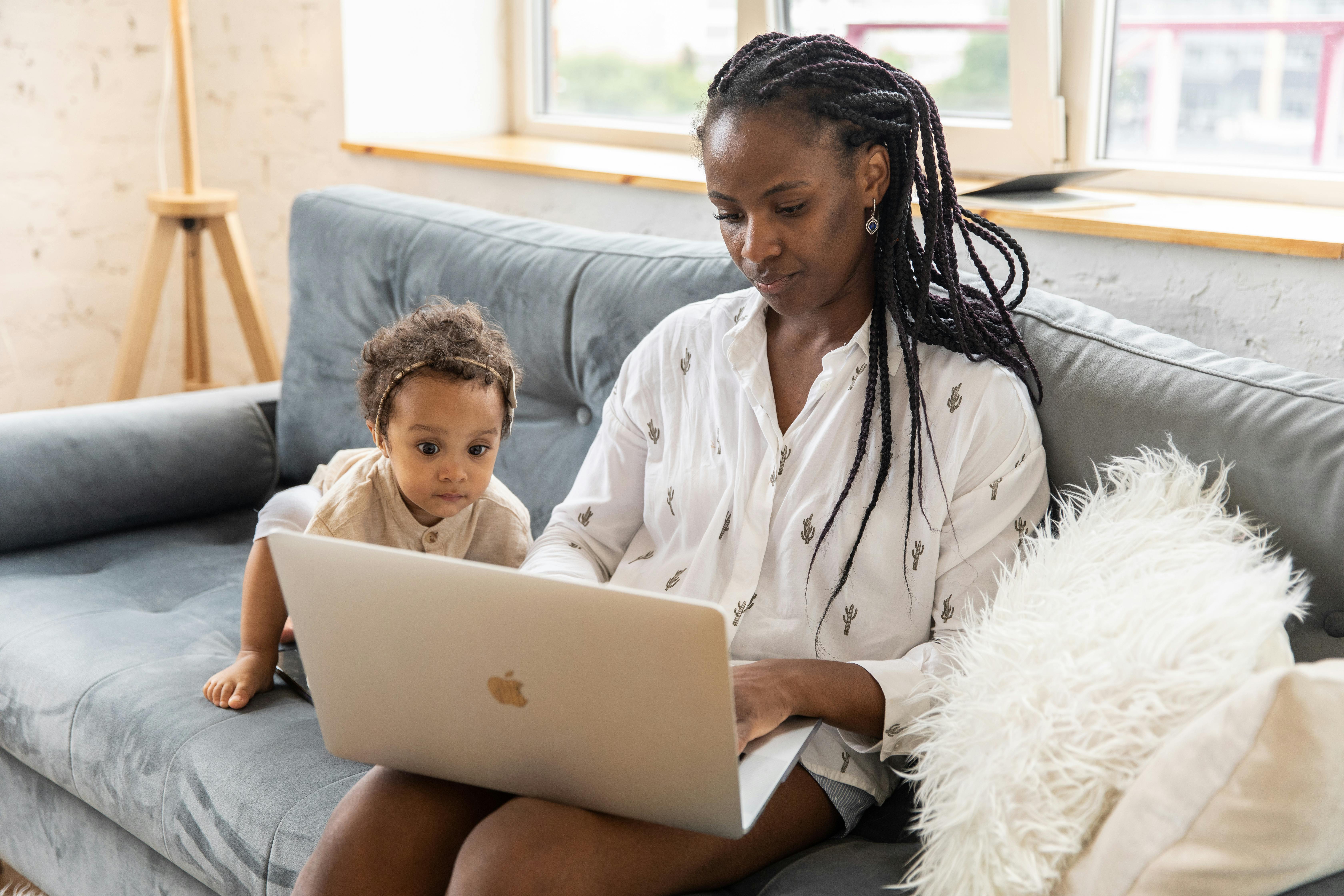Mother and baby sitting on the sofa using a laptop together indoors, showcasing modern family life.