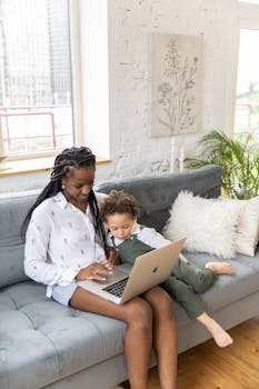 在明亮的客厅里，母亲和孩子舒适地坐在沙发上，与笔记本电脑互动