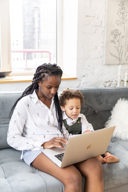 A mother and child sit together using a laptop indoors with natural lighting.