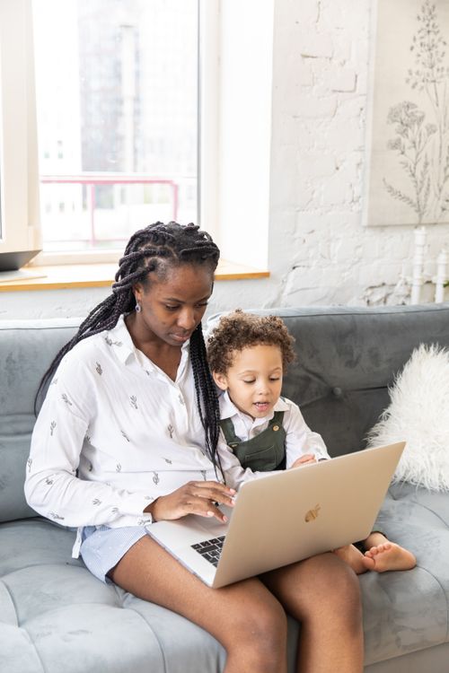 Free A mother and child sit together using a laptop indoors with natural lighting. Stock Photo