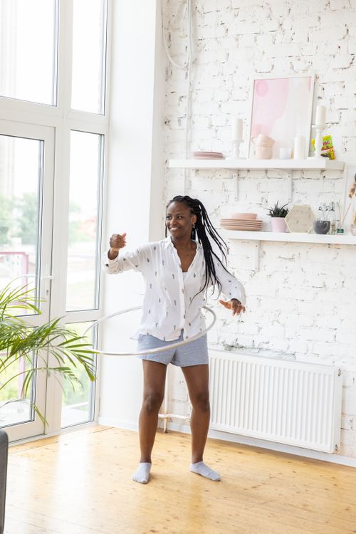 Free Smiling woman with long hair hula hooping in a bright room with stylish decor. Stock Photo