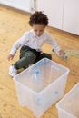 Boy in White Long Sleeve Shirt and Black Pants Sitting on Plastic Container
