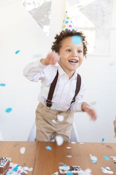 一个快乐的孩子戴着派对帽子，在室内用五彩纸屑庆祝