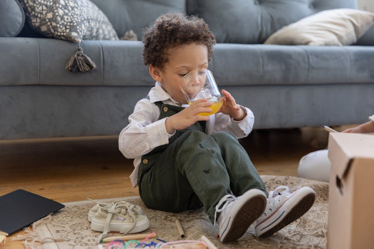 Little Boy Sitting On Ground Drinking Juice