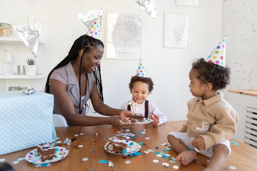 Mother and children celebrating a birthday indoors with cake and party hats. Joyful and lively atmosphere.
