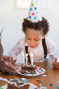 Young child celebrating birthday by blowing out candles on a chocolate cake.