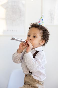 可爱的孩子在室内戴着生日帽吹着派对喇叭欢庆