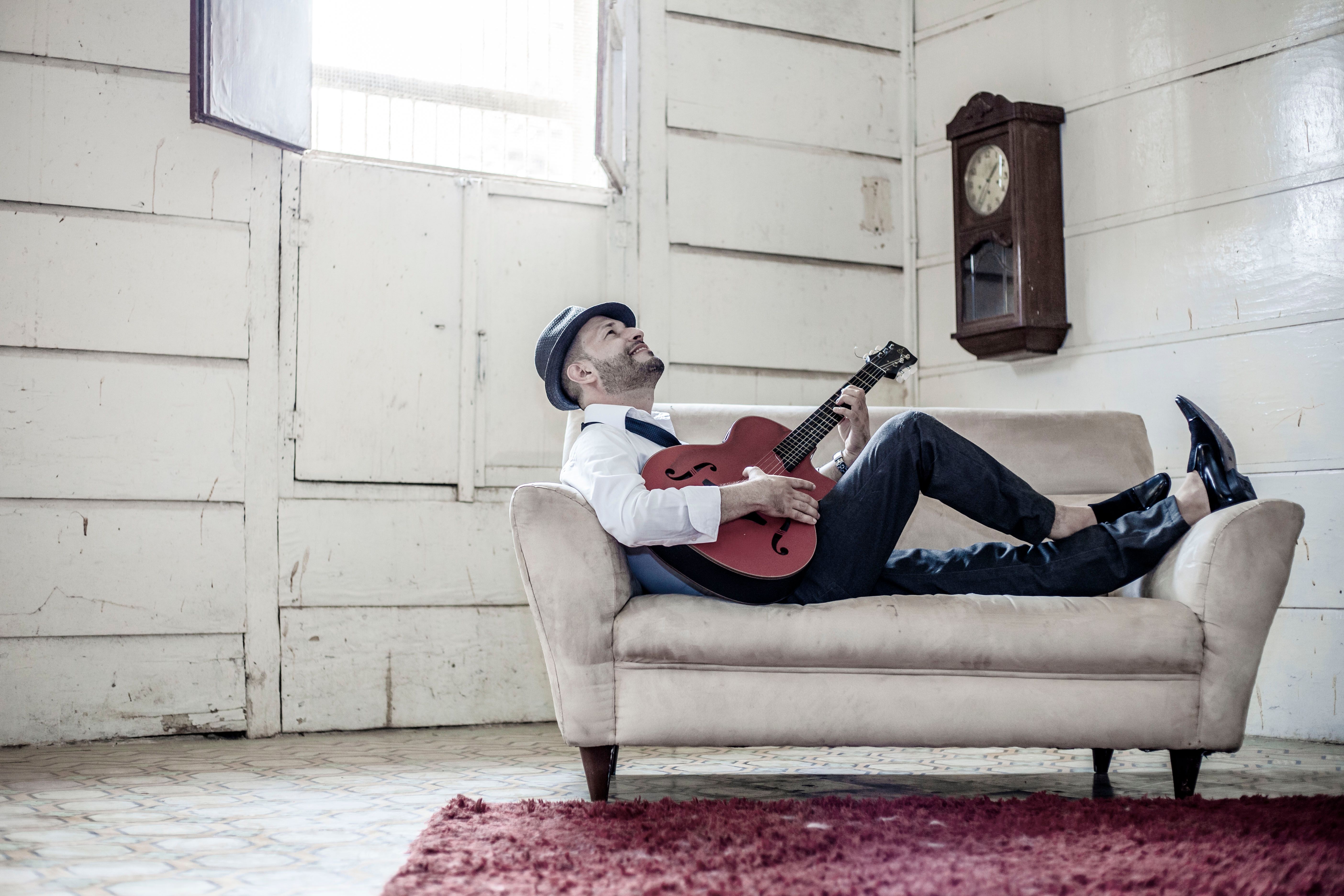 A Man Playing the Guitar while Sitting on a Couch · Free Stock Photo