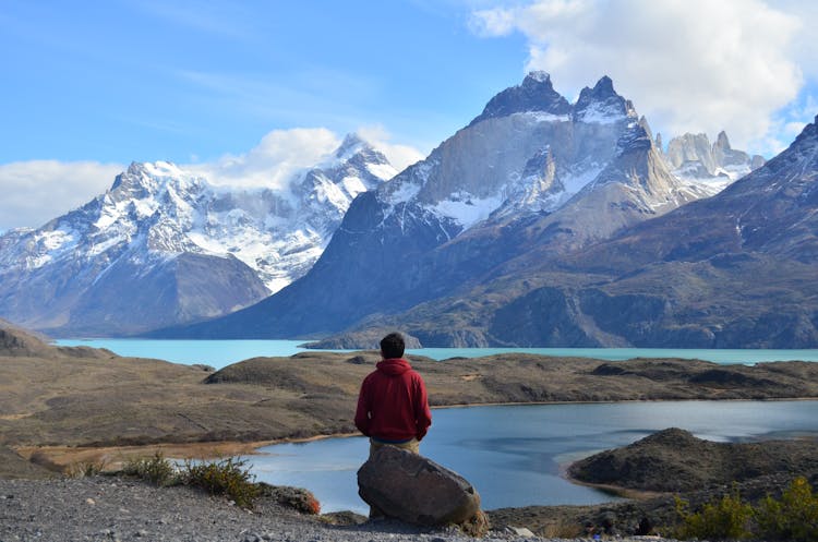 Man In Red Hoodie Sitting On Rock Near Lake