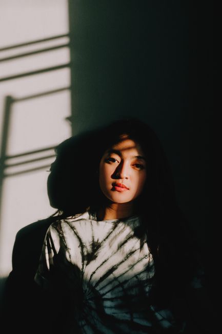 Artistic portrait of a young woman with light and shadow patterns, creating a moody atmosphere.