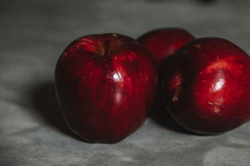 Free Three vibrant red apples photographed close-up against a neutral gray background, highlighting their glossy skin. Stock Photo
