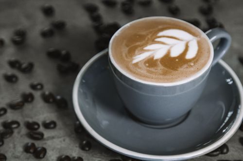 Free Close-up of a latte with art in a gray ceramic mug surrounded by coffee beans. Stock Photo
