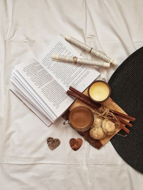 A warm and cozy still life featuring an open book, coffee, candle, and cookies on a rustic setup.
