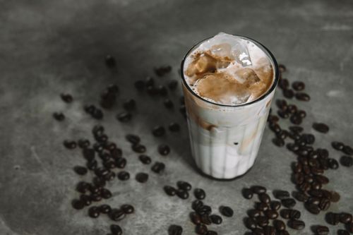 Free Refreshing iced coffee with milk and ice cubes surrounded by coffee beans on a rustic surface. Stock Photo