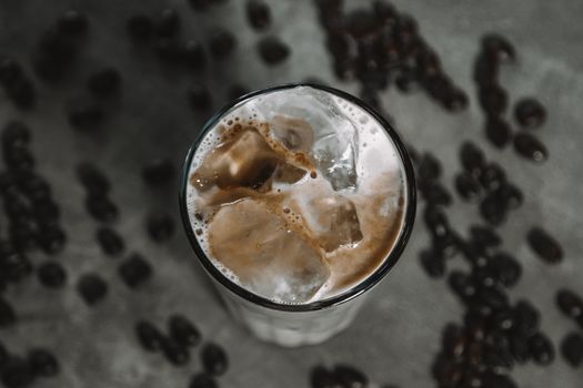 Top view of a refreshing iced coffee with creamy froth and scattered coffee beans on a rustic background.