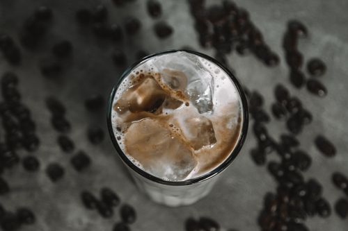 Free Top view of a refreshing iced coffee with creamy froth and scattered coffee beans on a rustic background. Stock Photo