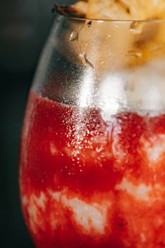 Extreme close-up of a vibrant red fruit slush drink with pineapple garnish.