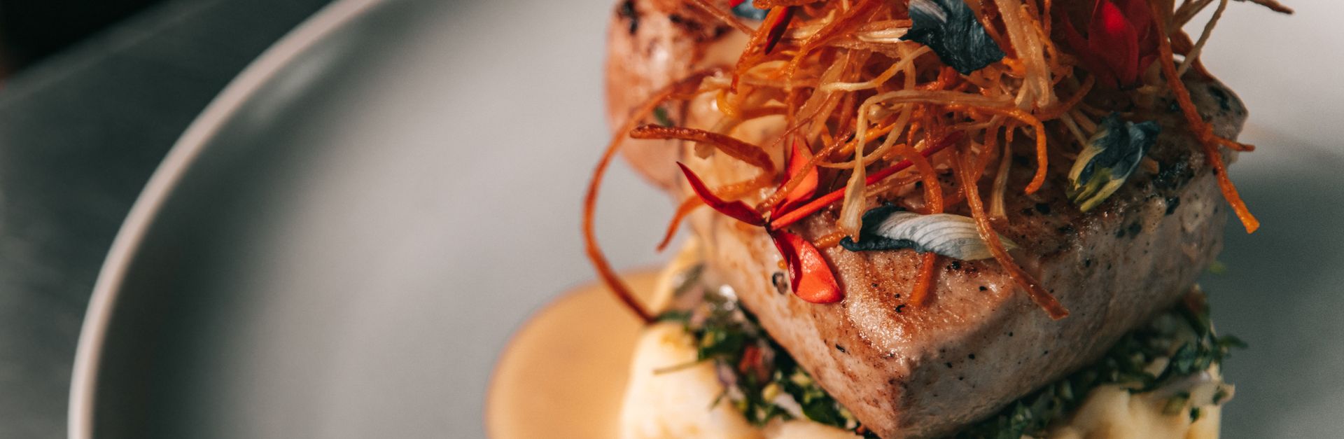 A gourmet tuna steak served on mashed potatoes with colorful garnish on a white plate.