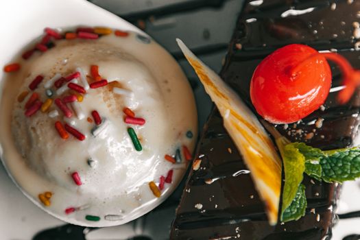 Delicious ice cream with sprinkles and chocolate dessert garnished with cherry and mint.