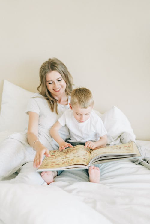 Free Woman In White Shirt Sitting On Bed Beside Her Child Stock Photo