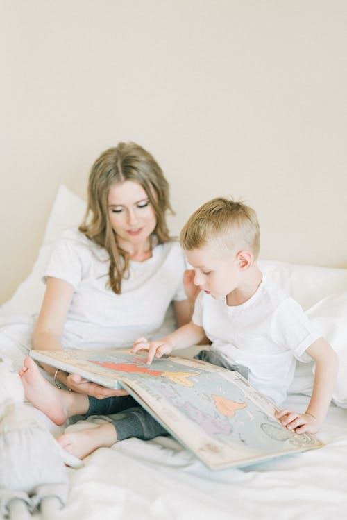 Free Woman In White Shirt Sitting Beside A Boy In White Shirt Reading Book Stock Photo