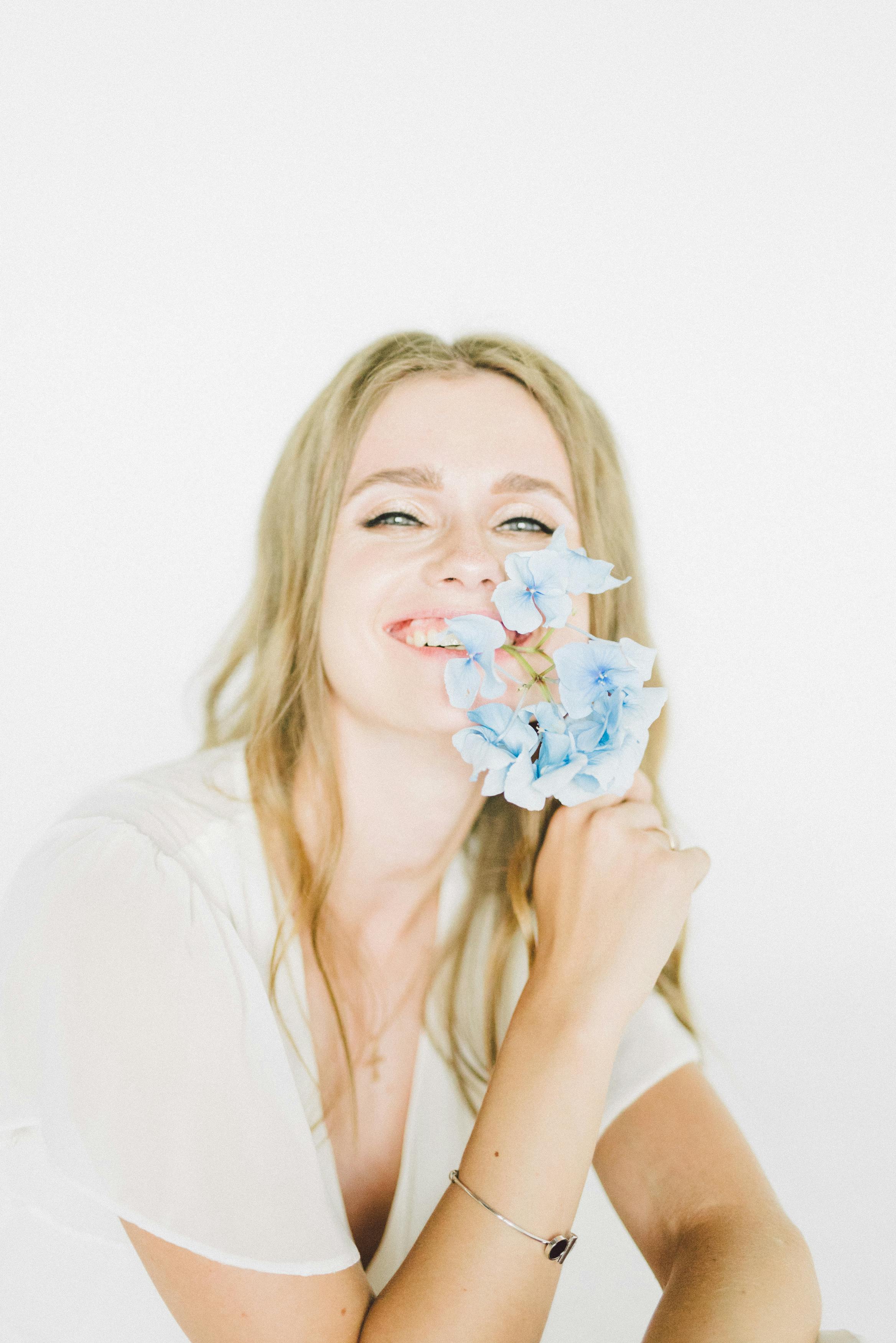 在柔和明亮的背景下，一个快乐的女人手持蓝色绣球花绽放