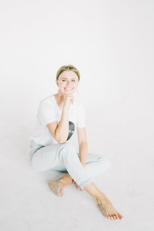 Woman In White Shirt And Jeans Sitting On White Floor