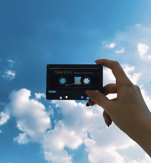 Crop woman showing old audio tape under shiny sky