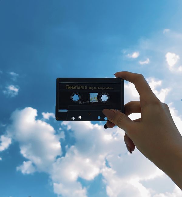 From below of crop unrecognizable female demonstrating aged audio cassette under blue cloudy sky in sunlight