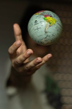 A hand reaching out towards a small floating globe, showing a close-up perspective. 4870334