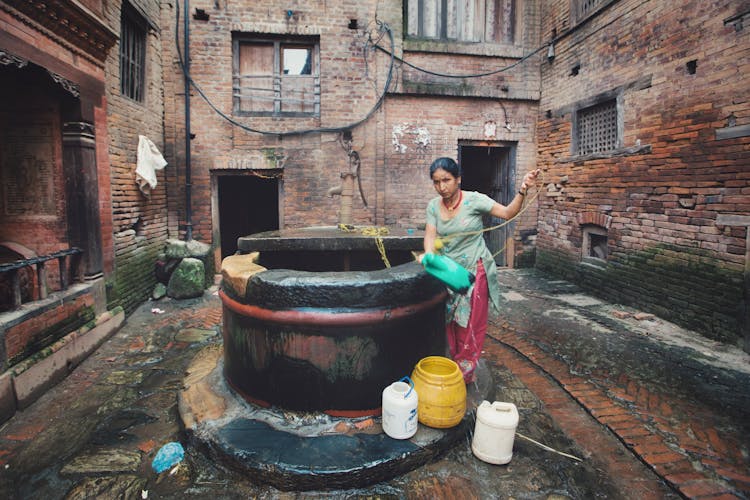 Ethnic Woman Pouring Water In Bucket