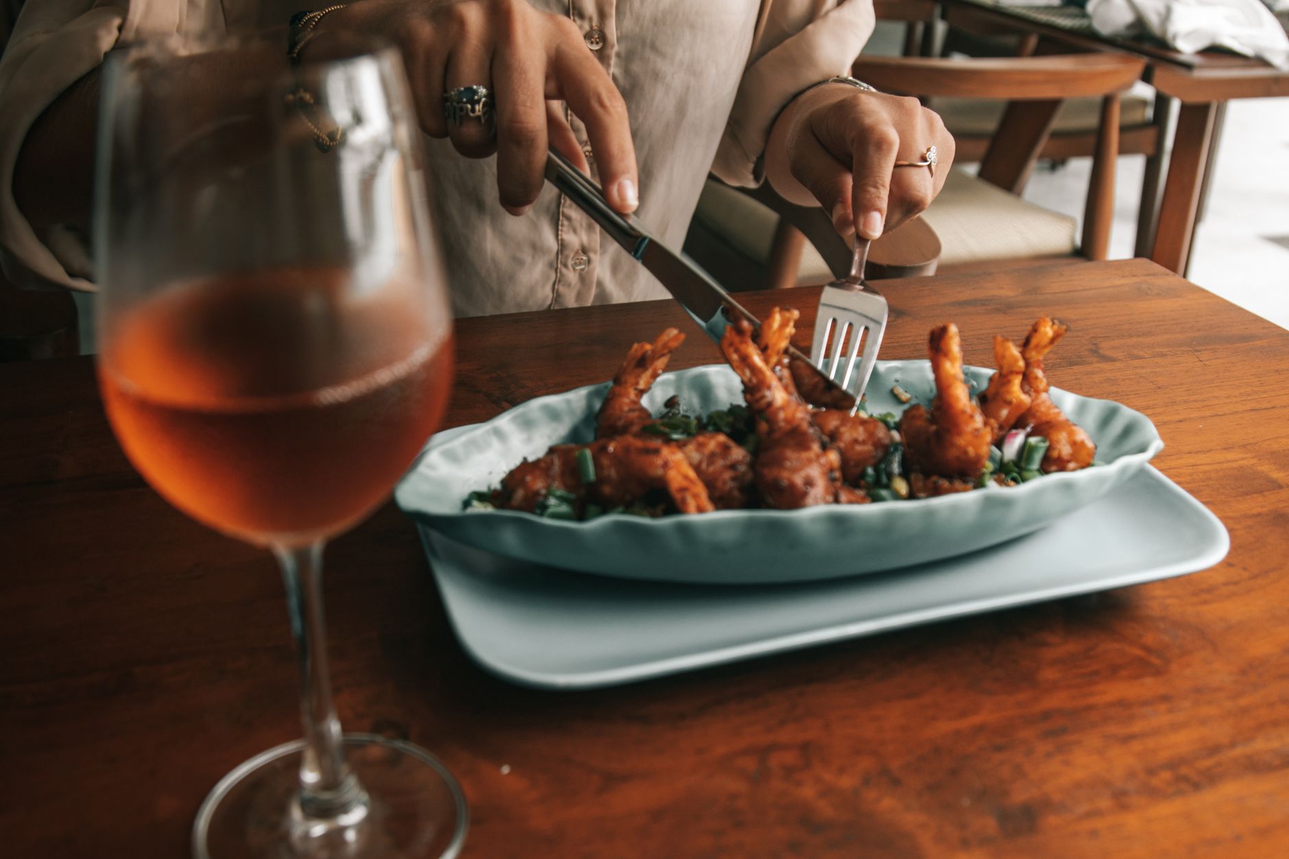A chilled glass of pale rosé wine positioned beside a plate of spiced seafood on a white linen table.