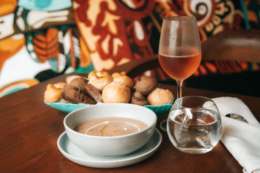 Elegant setup of breads, soup, and rose wine on a wooden table with a vibrant backdrop.