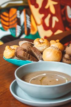 Close-up of a bowl of soup served with an assortment of artisan breads on a wooden table.