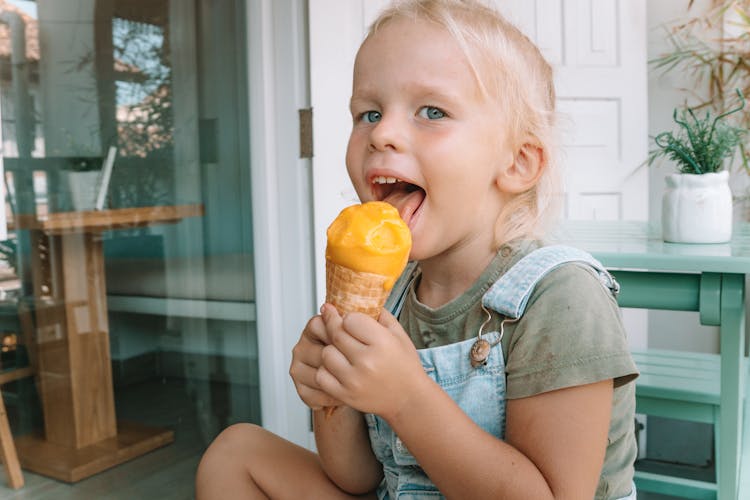 Girl In Denim Jumper Eating Yellow Ice Cream Cone