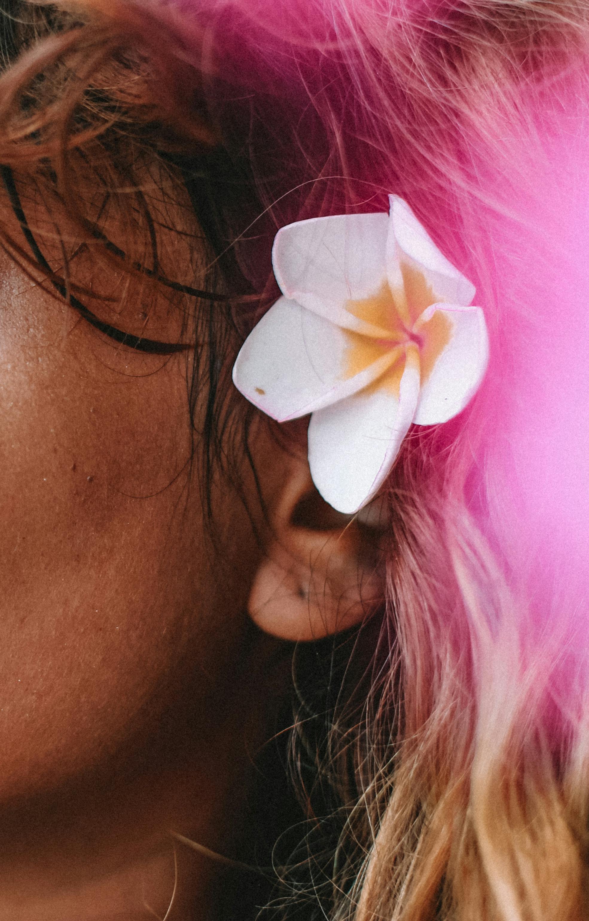 A close-up shot of a white frangipani flower tucked into a person's hair, showing natural beauty.