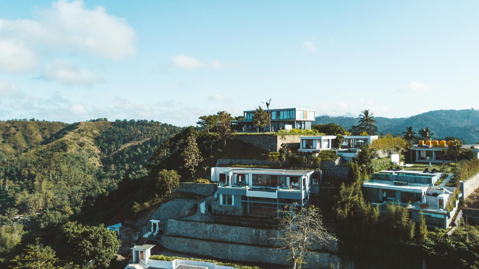 Luxury villas on a hillside overlooking lush green mountains and a clear blue sky.