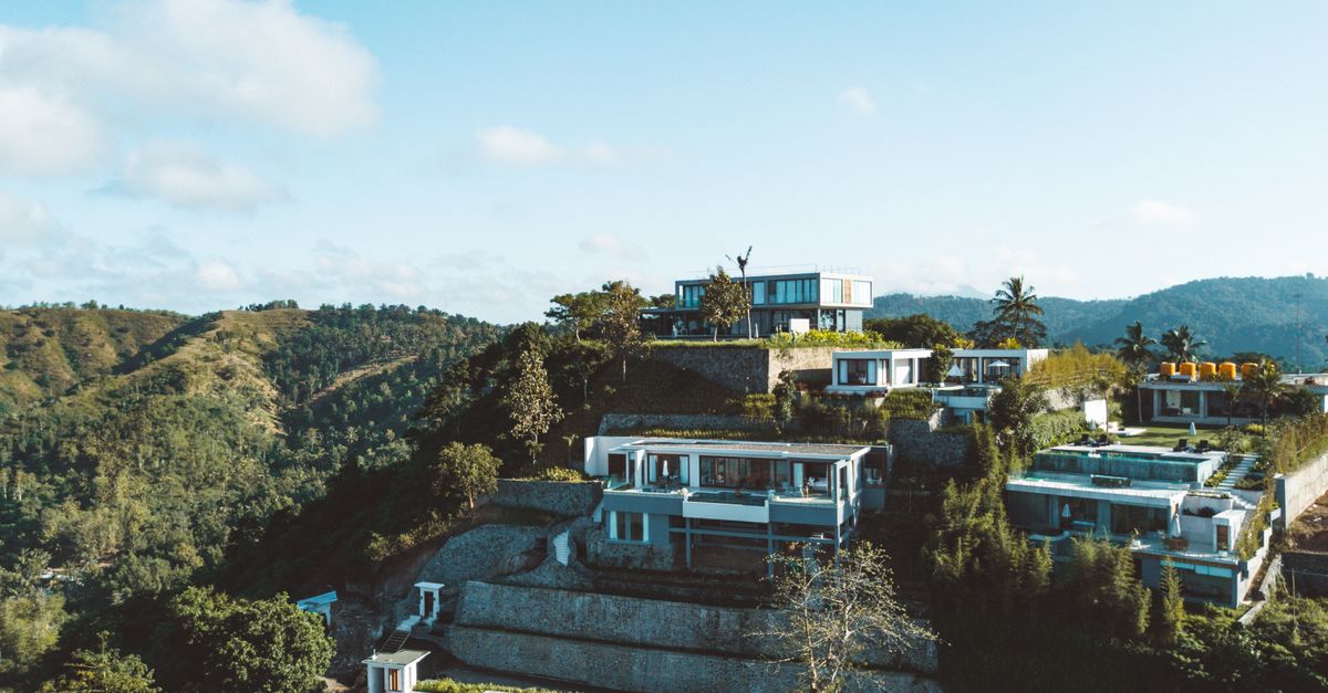 Luxury villas on a hillside overlooking lush green mountains and a clear blue sky.