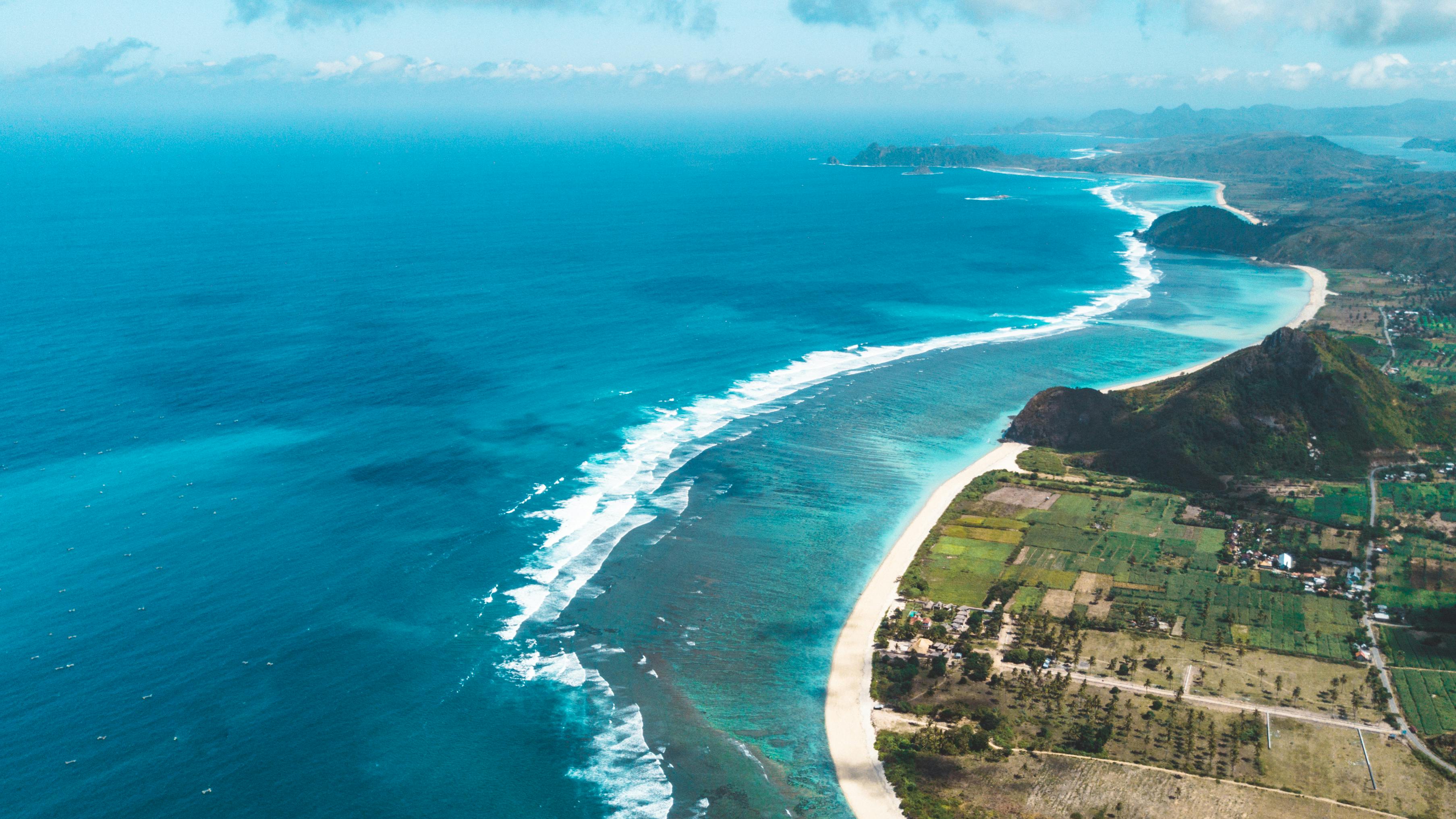 航拍照片令人惊叹，海岸线上是清澈的蓝色海洋和绿色的田野