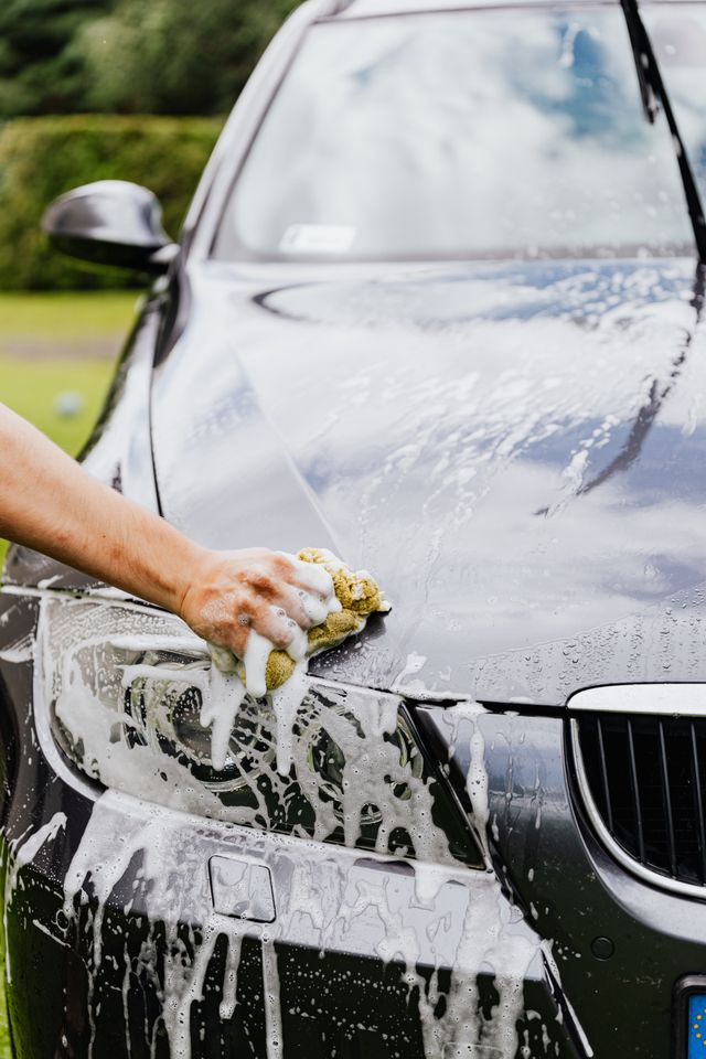 Worker hand-washing a black car with foam