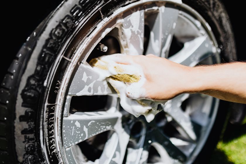 Hand scrubbing a car wheel rim with soap suds