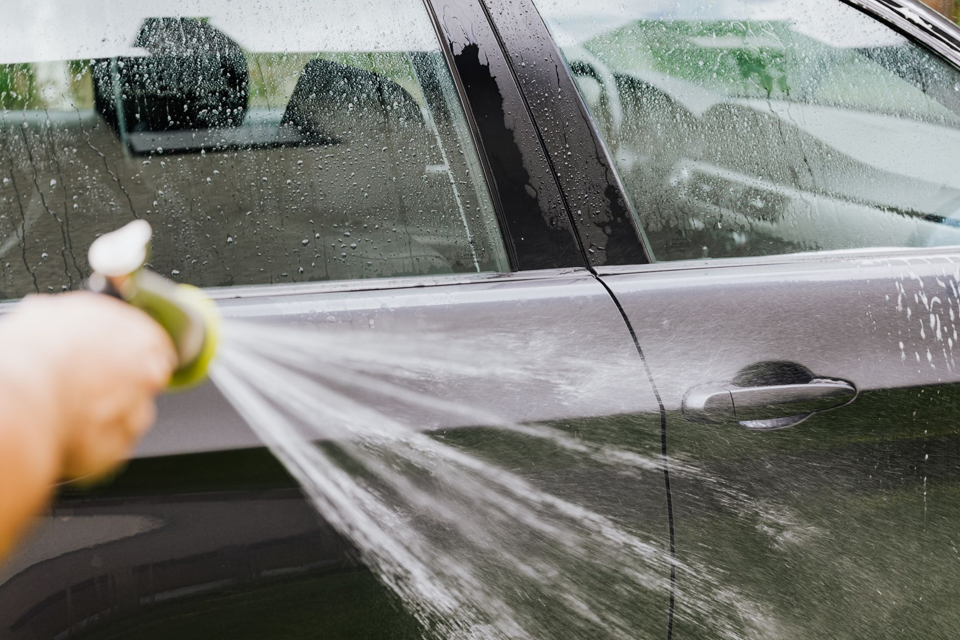 Rinsing sand from a black car with a hose