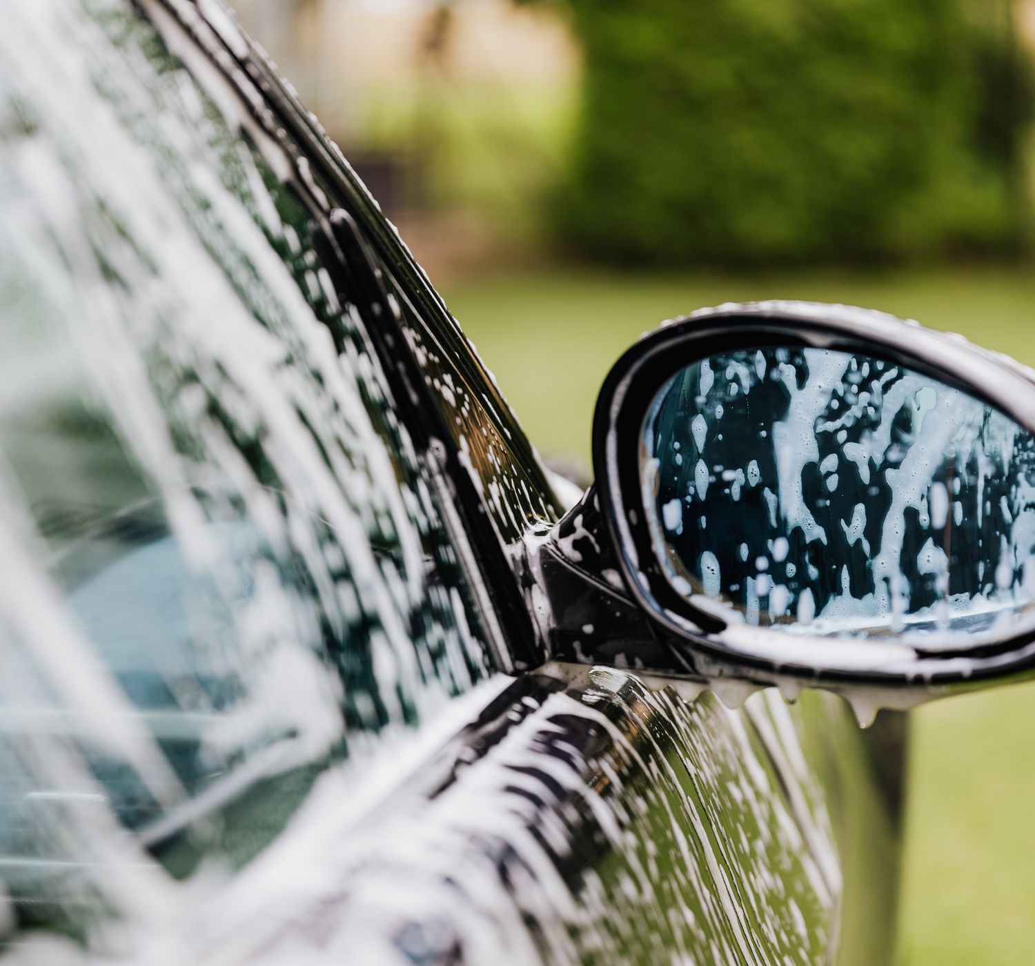 A detailed view of a car side mirror with soap suds, highlighting car wash detail.
