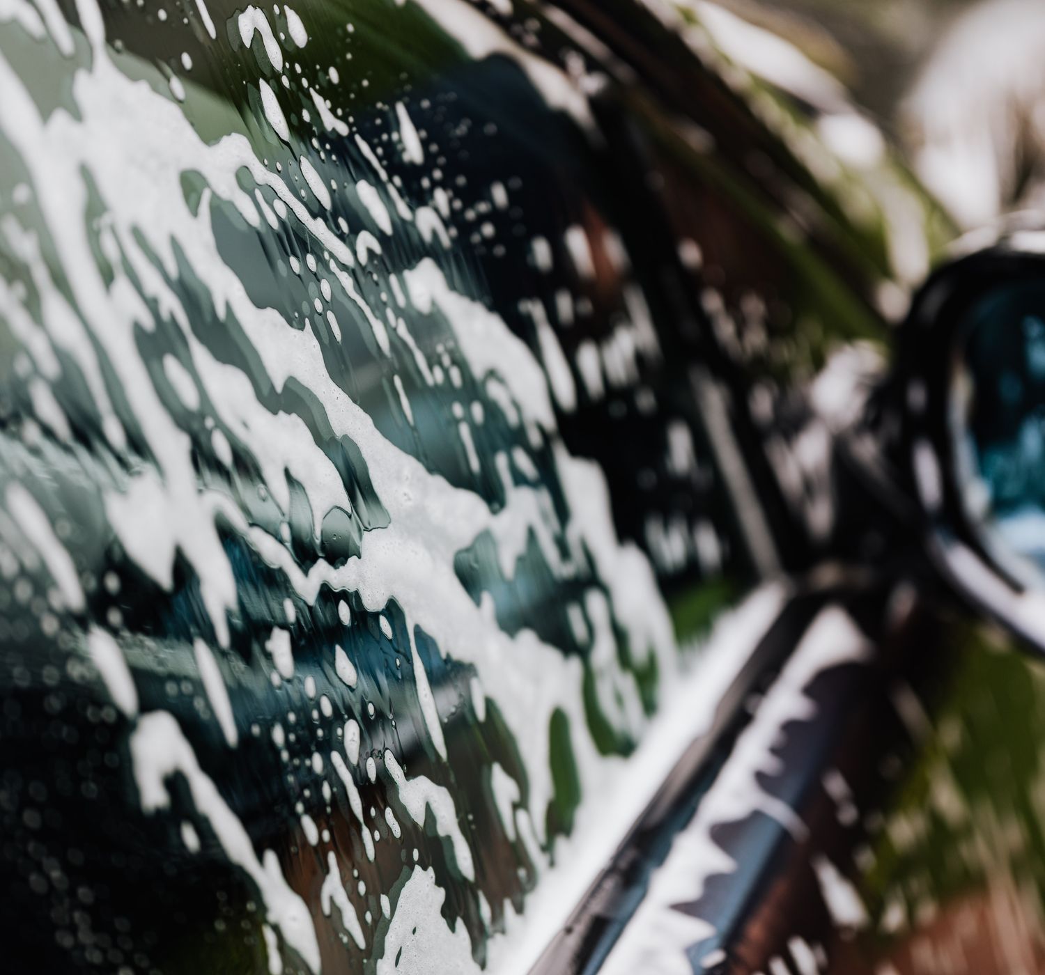 Detailed view of car covered in soapy foam during a wash, highlighting cleanliness.