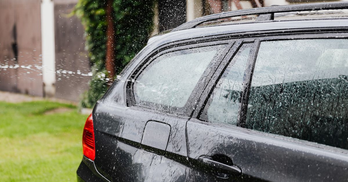 Side view of a black car being washed with water spraying in an outdoor setting.