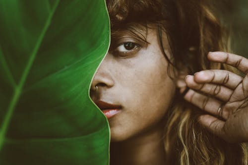 Close-Up Photo of a Woman with a Nose Piercing Beside a Green Leaf