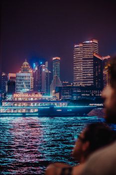 夜晚，游船穿过黄浦江，上海浦东区的天际线被灯光照亮